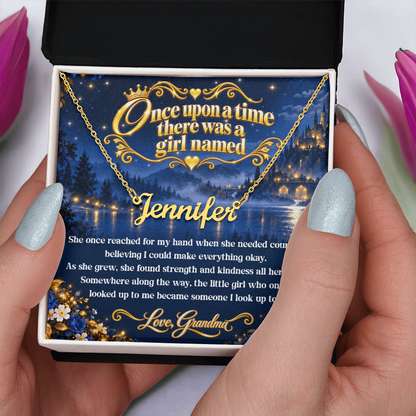 Hands holding an open black and white gift box with a gold-tone Jennifer name necklace and fairy-tale card from Grandma.